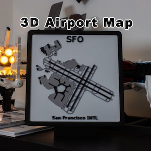 May include: A square 3D airport map display featuring the SFO San Francisco INTL layout. The map has a white background with black and gray raised runway and terminal details, framed in a black border. The text 3D Airport Map is visible above.