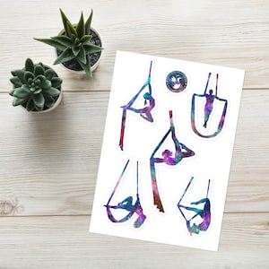 Op de afbeelding: Een vel stickers met kleurrijke, galaxy-thema illustraties van mensen die aan aerial silks doen. De stickers zijn wit met een glanzende afwerking.