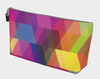 May include: A rectangular cosmetic bag with a vibrant geometric pattern in shades of pink, purple, blue, orange, and yellow. The bag has a silver zipper closure and a small black tab attached to the zipper.