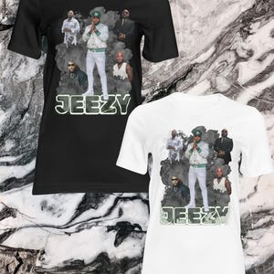 May include: Two t-shirts, one black and one white, each featuring a graphic of a group of people and the name "JEEZY" in a green and white font. The graphic includes a central figure in a white jacket and pants.
