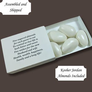 May include: A white matchbox-style box with a white lid. The lid has a printed message about five sugared almonds and wishes for a happy life. The box is open and contains five white Jordan almonds. The text on the bottom of the box reads "Kosher Jordan Almonds Included."