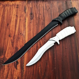 May include: Two knives on a wooden surface. One is a long, black blade with a black handle. The other is a shorter, curved blade with a white handle. The blades are sharp and the handles appear to be wrapped.