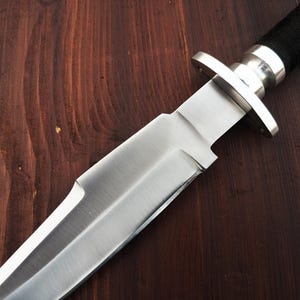 May include: A close-up of a silver knife with a black handle. The knife is sharp and has a pointed tip. The blade is smooth and shiny.