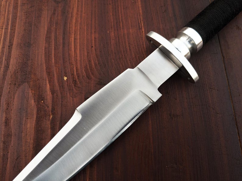 May include: A close-up of a silver knife with a black handle. The knife is sharp and has a pointed tip. The blade is smooth and shiny.