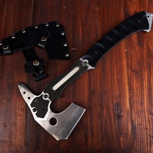 May include: A tactical tomahawk with a black handle and silver blade, alongside a black leather sheath. The axe has a sharp blade and a textured grip for secure handling. The tomahawk is designed for outdoor use.