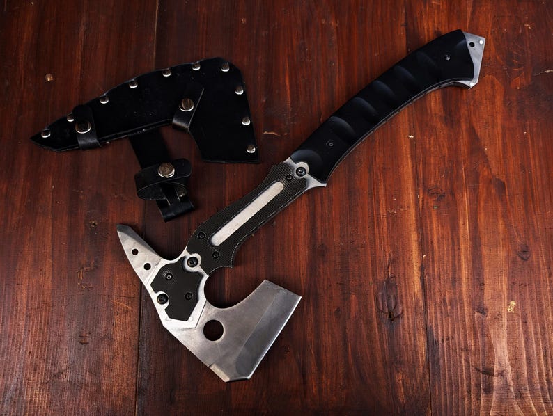 May include: A tactical tomahawk with a black handle and silver blade, alongside a black leather sheath. The axe has a sharp blade and a textured grip for secure handling. The tomahawk is designed for outdoor use.