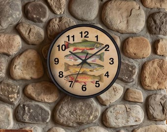 May include: A round wall clock with a black frame and a beige face featuring illustrations of four different fish species. The clock has black hour, minute, and second hands, and black Arabic numerals from one to twelve around the perimeter.