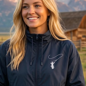 May include: A navy blue zip-up windbreaker jacket featuring a high collar with drawstring cords and a white graphic print on the left chest depicting a person using a lasso. The jacket has long sleeves with elastic cuffs and a front zipper closure.