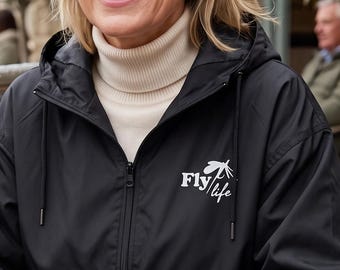 May include: A black hooded windbreaker jacket featuring a white logo on the chest that reads Fly Life, worn over a cream-colored turtleneck sweater. The jacket has a full-length front zipper, long sleeves with elastic cuffs, and a drawstring hood.