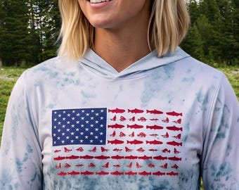 May include: A long-sleeve hooded shirt with a blue and white tie-dye pattern. The center features a graphic of the American flag, where the stripes are composed of small red fish silhouettes and the blue field contains white stars.