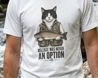 May include: A white short-sleeved t-shirt featuring a graphic of a black and white cat wearing a fishing vest and holding a fish. Below the cat, the text reads "RELEASE WAS NEVER AN OPTION" in bold, dark lettering. The shirt has a crew neckline.