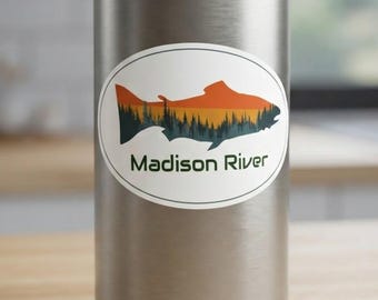 May include: A silver metal water bottle featuring an oval sticker. The sticker displays a fish silhouette filled with a sunset-colored sky over a dark forest landscape, with the text Madison River printed in dark green letters below the fish.