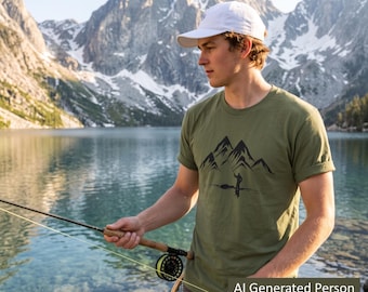 May include: An olive green short-sleeved t-shirt featuring a black graphic print of a mountain range and a person fishing. The shirt is paired with a white baseball cap. The graphic depicts a silhouette of a person standing by water.