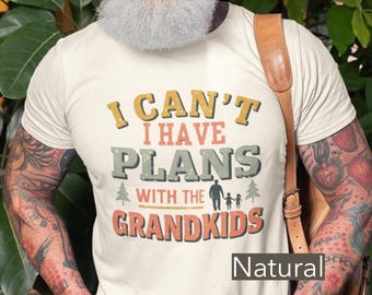Puede incluir: Camiseta color crema con el texto "I CAN'T I HAVE PLANS WITH THE GRANDKIDS" en varios tipos de letra y colores. La camiseta presenta una silueta familiar y árboles. La palabra "Natural" está debajo.