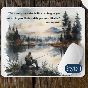 Könnte beinhalten: Eine Aquarell-Illustration eines Mannes, der an einem See in einem Wald angelt. Der Spruch "The trout do not rise in the cemetery, so you better do your fishing while you are still able." ist auf der Mausmatte gedruckt. Die Texte "Sparse Grey Hackle" und "Style 1" sind ebenfalls auf der Mausmatte gedruckt.