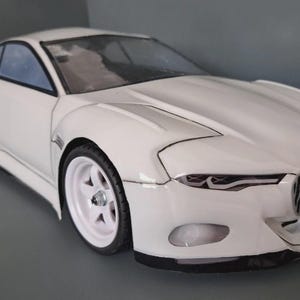 May include: A white model car with a sleek, aerodynamic design. The car features white wheels, a spoiler, and a detailed front grille. The car's windows are tinted, and the body has sharp lines.