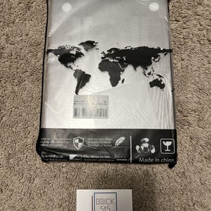 May include: A clear plastic case with a world map design for a laptop. The case is thin and light, and has vents for heat dissipation. The case is made in China. The text "BRICK 515 COLLECTIBLES" is on a white card in the bottom right corner of the image.