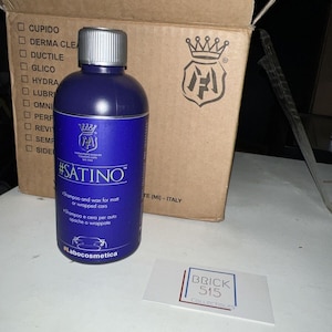 May include: A dark blue bottle of #SATINO shampoo and wax for matte or wrapped cars. The bottle has a silver cap and white text. A cardboard box with a logo is in the background, along with a business card that says BRICK 515 COLLECTIBLES.
