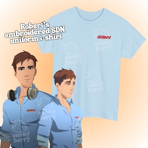 May include: Light blue t-shirt with the text "Robert's embroidered SDN uniform t-shirt". The shirt features the "emmy berry" logo and a strawberry pattern. The image also shows a cartoon illustration of a person wearing a blue shirt.