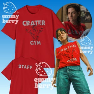 Op de afbeelding: Rode t-shirts met de tekst "CRATER GYM" en een afbeelding van een gespierde figuur. Eén shirt heeft "STAFF" op de achterkant gedrukt. De afbeelding bevat een persoon die een rode tanktop met hetzelfde ontwerp draagt.