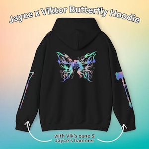 May include: Black hoodie with a holographic butterfly design on the back. The sleeves feature a holographic cane and hammer design. "Jayce x Viktor Butterfly Hoodie" is written at the top of the image. "with Vik's cane & Jayce's hammer" is written at the bottom of the image.