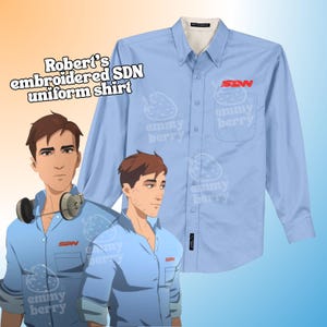 Puede incluir: Camisa de uniforme azul claro con botones con el texto "Robert's embroidered SDN uniform shirt" y el logotipo de SDN en rojo. La camisa tiene un bolsillo con el logotipo "emmy berry" y un diseño de fresa.