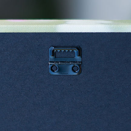 May include: Close-up of the back of a canvas art piece. A black metal sawtooth hanger is attached to the dark blue canvas backing. The canvas edge is visible, showing a light green and white pattern.