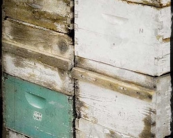 May include: A stack of wooden boxes, some painted white, some with a natural wood finish. The top box has a green painted section with the words "Fisher Honey" written on it.