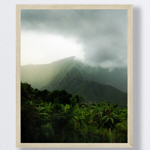 May include: A photograph of a lush green mountain range with a thick layer of clouds covering the peaks. The mountainside is covered in dense foliage and trees.