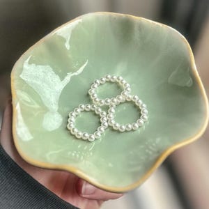 May include: Three pearl rings on a green ceramic dish with a wavy edge.