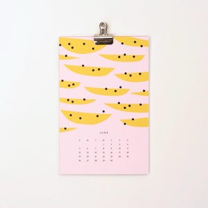 May include: A pink calendar with a June header and a yellow and black watermelon pattern. The calendar is hanging from a silver clip.