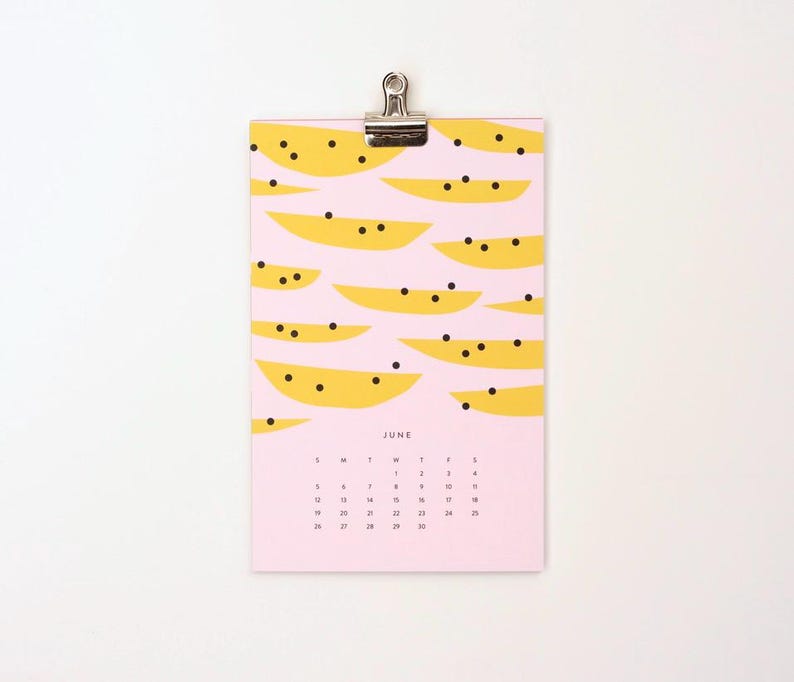 May include: A pink calendar with a June header and a yellow and black watermelon pattern. The calendar is hanging from a silver clip.