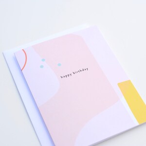 May include: A pink and white greeting card with abstract shapes and blue dots. The card says "happy birthday" in black text.