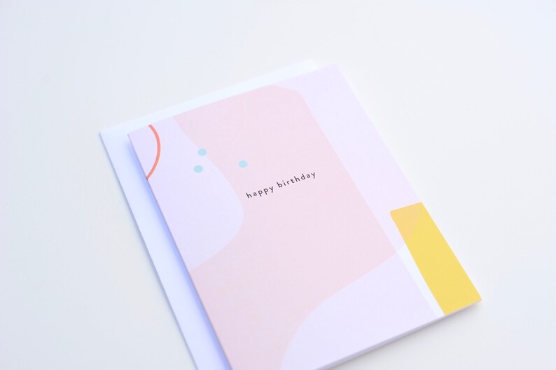 May include: A pink and white greeting card with abstract shapes and blue dots. The card says "happy birthday" in black text.