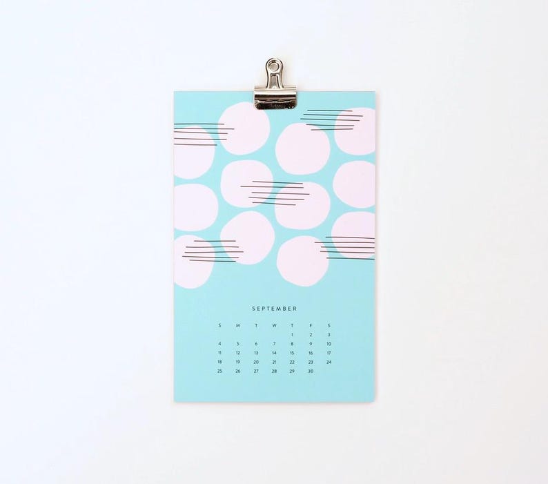 May include: A light blue calendar with a pink and black abstract design. The calendar is for September and has the days of the week and numbers for each day of the month.
