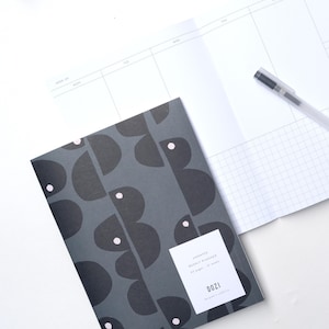 May include: A gray weekly planner with a geometric pattern of black and white shapes. The cover has the text "UNDATED WEEKLY PLANNER 52 pages - 52 weeks" and "DOZI The good in simple".
