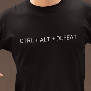 May include: Black t-shirt with white text that reads "CTRL + ALT + DEFEAT".