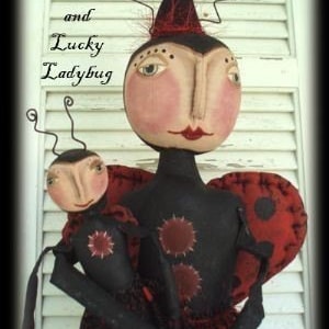 May include: Two handmade fabric dolls dressed as ladybugs. The larger ladybug doll is wearing a red hat and has a black and red polka dot dress. The smaller ladybug doll is wearing a black and red polka dot dress. The dolls are holding each other and have painted faces.