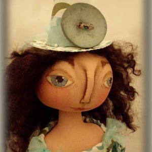 May include: A doll with brown curly hair wearing a blue and white patterned dress and a blue and white hat with a large blue button. The doll has a painted face with blue eyes and a large nose.