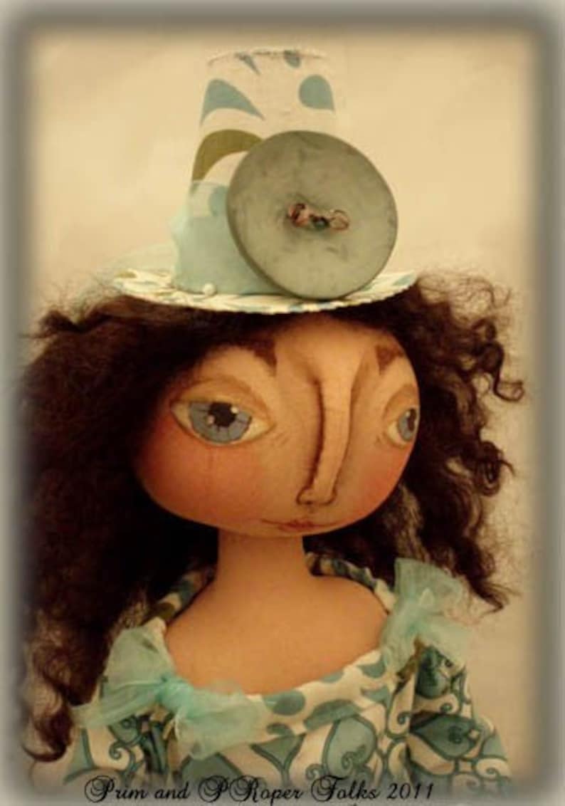 May include: A doll with brown curly hair wearing a blue and white patterned dress and a blue and white hat with a large blue button. The doll has a painted face with blue eyes and a large nose.
