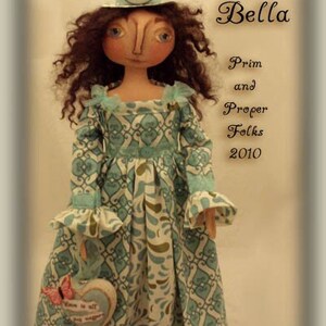 May include: A handmade doll called Bella, wearing a blue and white patterned dress and a blue and white hat. The doll is holding a heart-shaped object with the text "Love is all" on it. The doll is part of the Prim and Proper Folks collection from 2010.