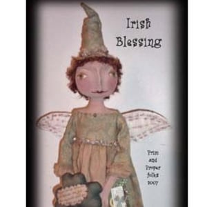 Puede incluir: Una muñeca hecha a mano con un vestido verde, un sombrero verde y alas. Lleva un trébol de cuatro hojas y un libro con las palabras "Irish Blessing" en la portada.