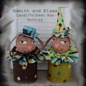 Puede incluir: Dos cajas de dulces o de chucherías con forma de conejo con detalles de tela marrón, verde y azul. Las cajas están etiquetadas como "Emmitt and Elsee Candy/Trinket Box Bunnies".