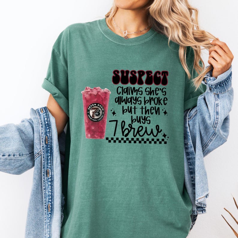 May include: A teal-colored t-shirt with the text "SUSPECT Claims she's always broke but then buys 7 Brew." A graphic of a red drink in a clear cup is on the left side of the text.
