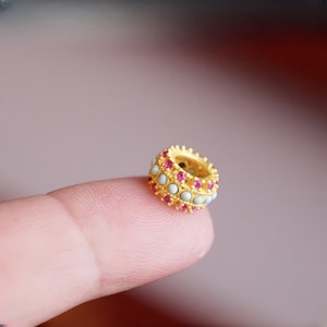May include: A gold ring with a band of white and pink stones. The ring is on a finger.