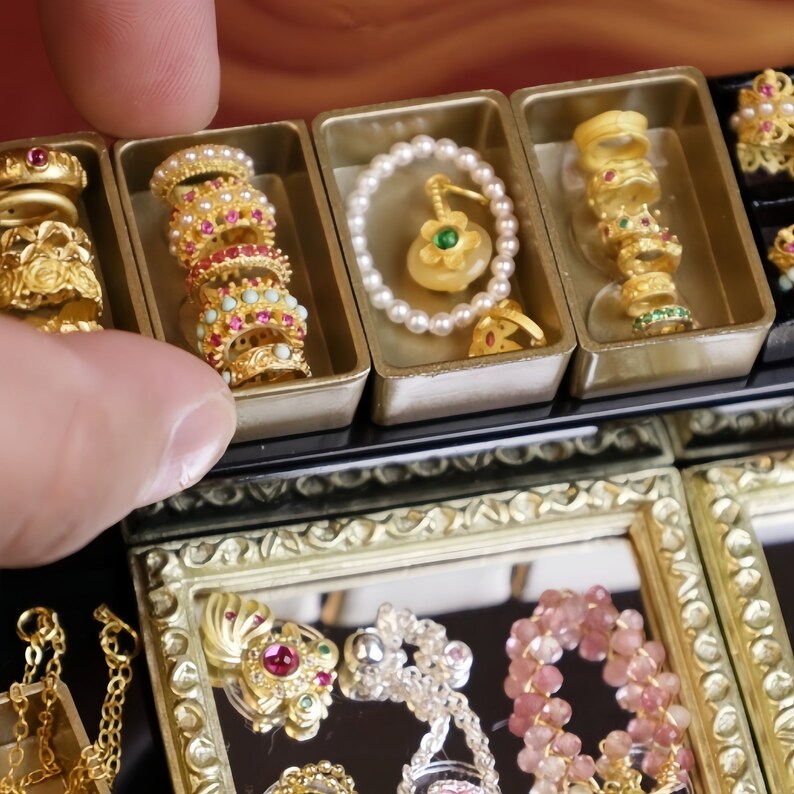 May include: A close-up of a jewelry display case with multiple compartments. Each compartment contains a variety of gold and silver jewelry, including rings, necklaces, and bracelets. Some of the jewelry is decorated with colorful gemstones.