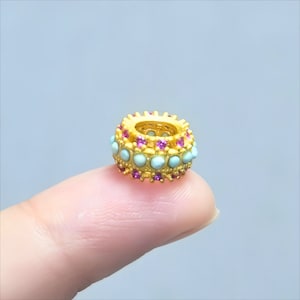 May include: A gold ring with a double row of light blue and pink gemstones. The ring is on a finger.