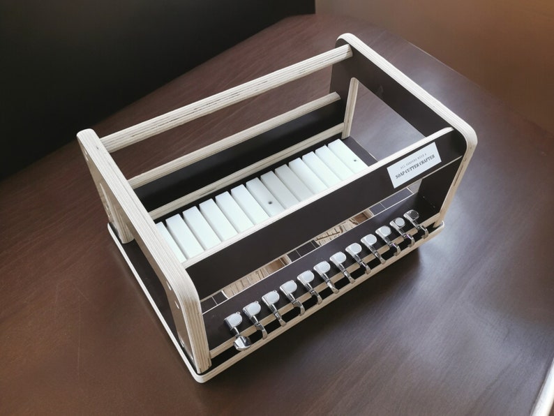May include: A wooden guitar tuner holder with a white plastic rack for storing guitar tuners. The holder has a black painted surface and a label that reads "SNAP GUTTER PAINTER".