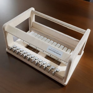 May include: A wooden soap cutter crafter with a white label that reads "ALL NATURAL HANDMADE SOAP CUTTER CRAFTERS". The cutter has a series of metal blades and a wooden frame.