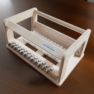 May include: A wooden soap cutter crafter with a white label that reads "ALL NATURAL HANDMADE SOAP CUTTER CRAFTERS". The cutter has a series of metal blades and a wooden frame.